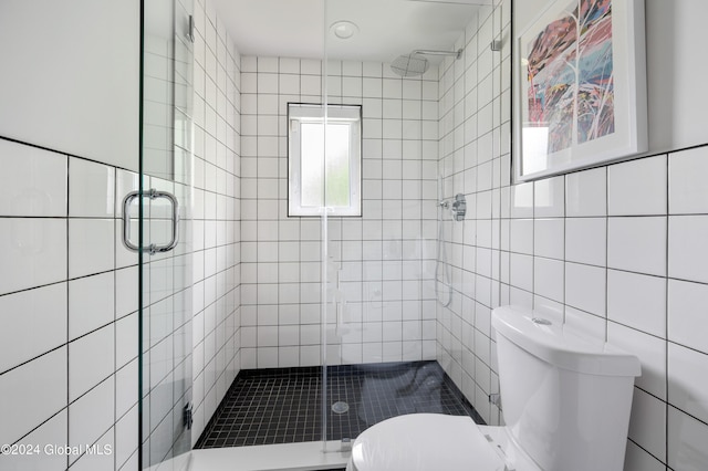 bathroom with toilet, a shower with door, and tile walls