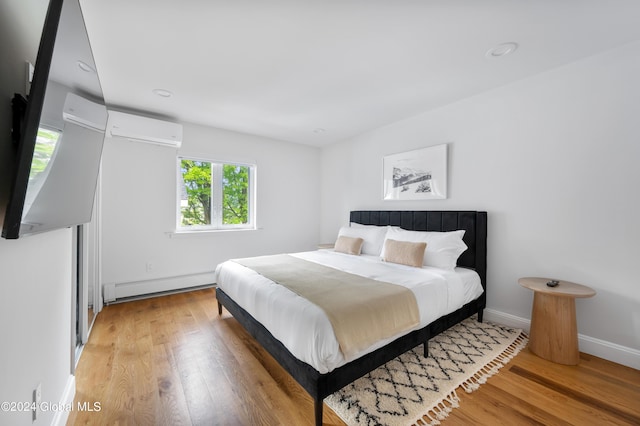 bedroom featuring baseboard heating, light hardwood / wood-style flooring, and an AC wall unit