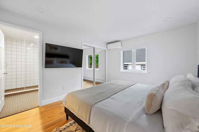 bedroom with a wall unit AC, connected bathroom, a closet, and hardwood / wood-style flooring