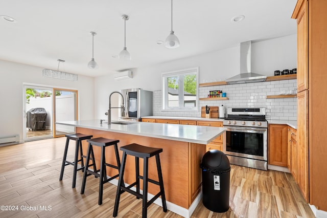 kitchen featuring a breakfast bar, a center island with sink, wall chimney range hood, appliances with stainless steel finishes, and a wall unit AC