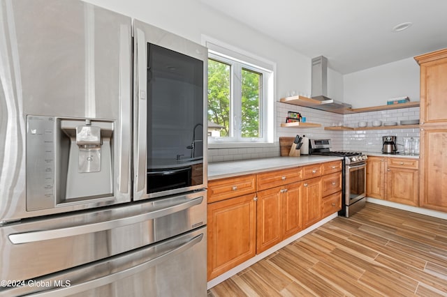 kitchen with decorative backsplash, stainless steel appliances, wall chimney range hood, and light hardwood / wood-style floors