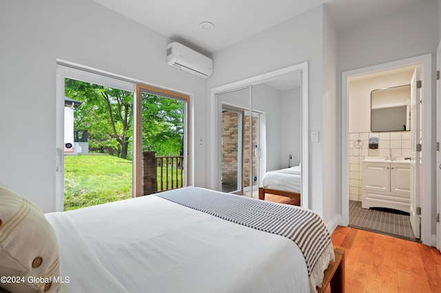 bedroom featuring hardwood / wood-style flooring, ensuite bathroom, access to exterior, and a wall unit AC