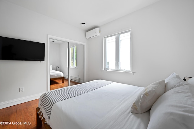 bedroom featuring hardwood / wood-style floors, baseboard heating, an AC wall unit, and a closet