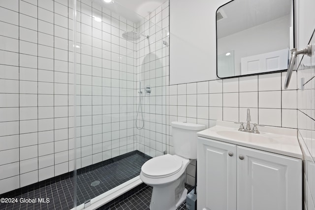 bathroom with vanity, tile patterned flooring, toilet, tiled shower, and tile walls