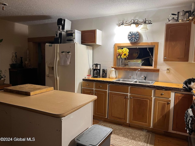 kitchen with white refrigerator with ice dispenser, a kitchen island, a textured ceiling, light hardwood / wood-style floors, and sink