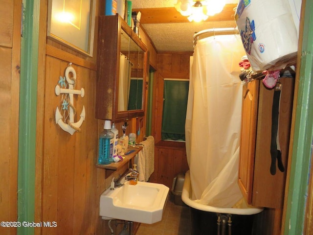 bathroom featuring a textured ceiling, wooden walls, and sink