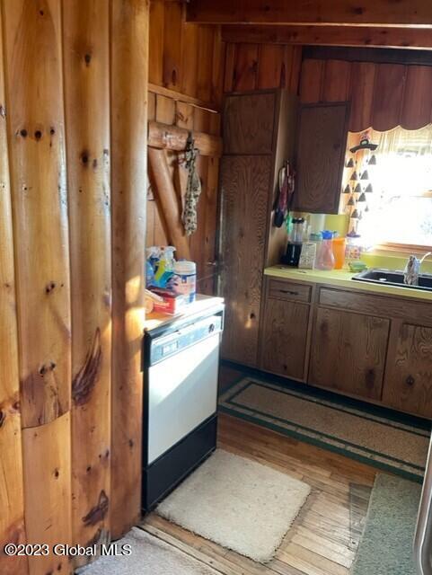 kitchen with dishwashing machine, wood finished floors, light countertops, wood walls, and a sink