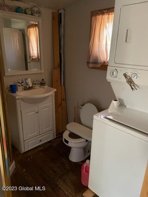 bathroom with stacked washing maching and dryer, vanity, hardwood / wood-style flooring, and toilet