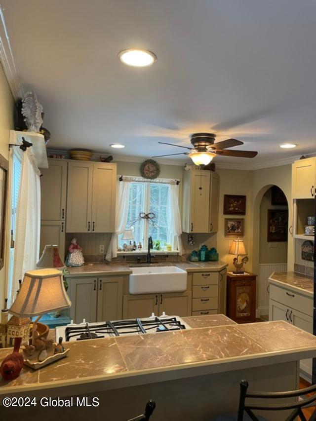 kitchen featuring backsplash, crown molding, gas stovetop, ceiling fan, and sink