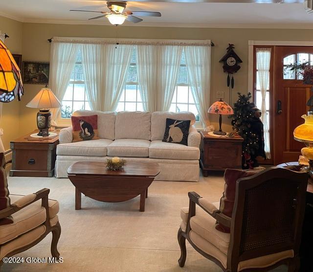 carpeted living room with ornamental molding and ceiling fan