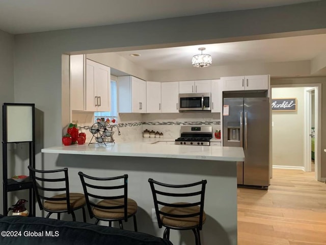 kitchen with kitchen peninsula, appliances with stainless steel finishes, a kitchen bar, white cabinetry, and light wood-type flooring