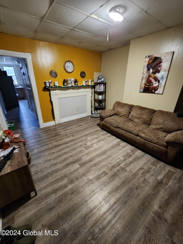 living room with a drop ceiling, dark hardwood / wood-style floors, and wooden walls