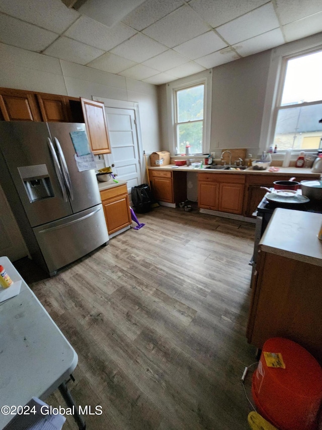 kitchen with light wood-type flooring, sink, a drop ceiling, and stainless steel refrigerator with ice dispenser