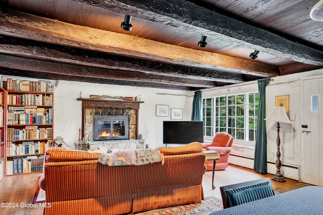 living room with beamed ceiling, wood ceiling, a stone fireplace, and hardwood / wood-style floors