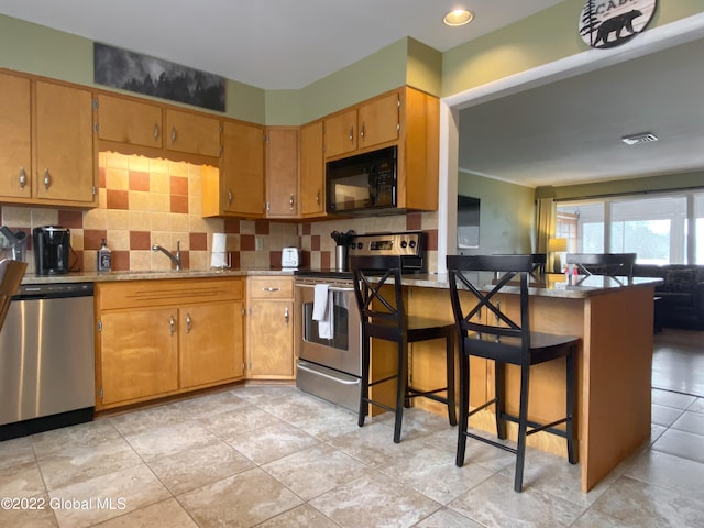 kitchen with tasteful backsplash, sink, kitchen peninsula, a kitchen breakfast bar, and stainless steel appliances