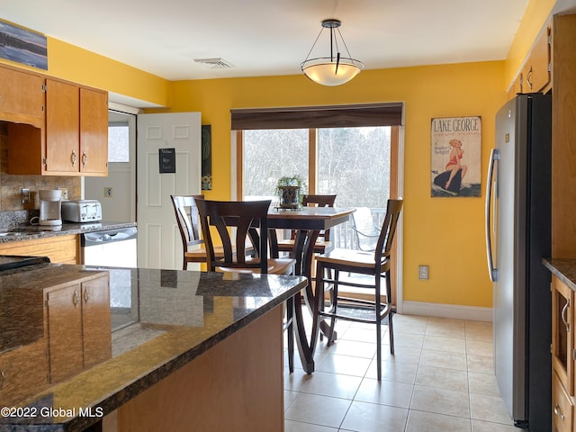 kitchen with pendant lighting, dark stone counters, decorative backsplash, appliances with stainless steel finishes, and light tile patterned floors