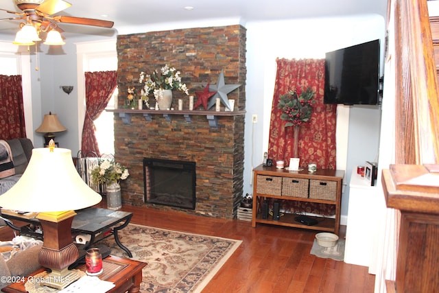 living room with a stone fireplace, dark hardwood / wood-style floors, and ceiling fan