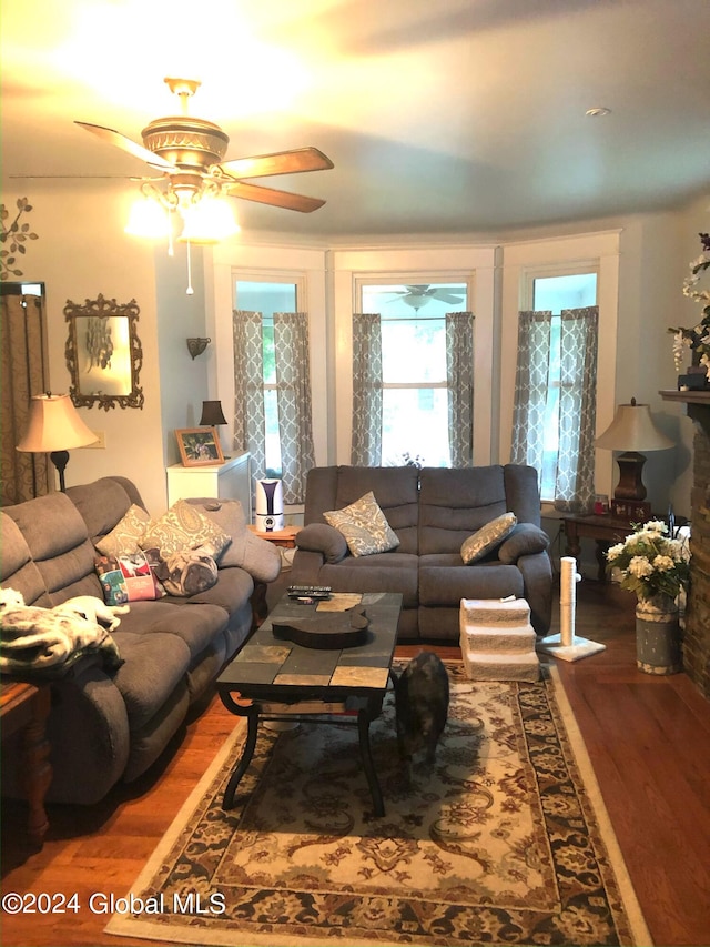 living room with dark hardwood / wood-style floors, ceiling fan, and a stone fireplace