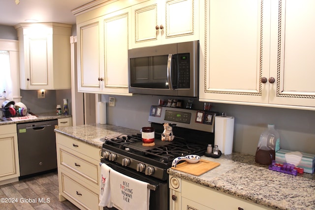 kitchen featuring stainless steel appliances, cream cabinets, light stone countertops, and light hardwood / wood-style flooring