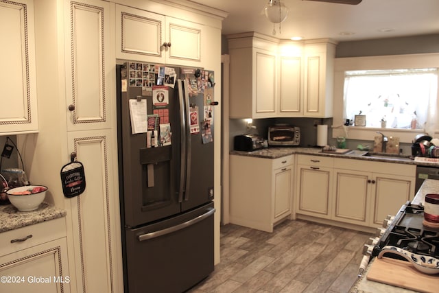 kitchen with dark stone counters, black refrigerator, light hardwood / wood-style flooring, ceiling fan, and sink