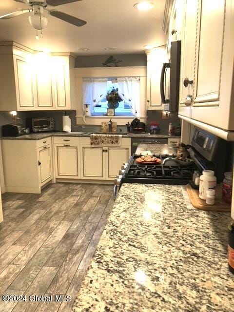 kitchen featuring dark stone counters, dark hardwood / wood-style floors, gas range oven, ceiling fan, and sink