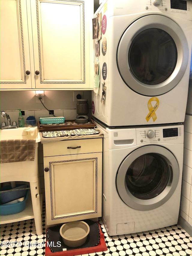 laundry room featuring light tile flooring, stacked washing maching and dryer, and cabinets