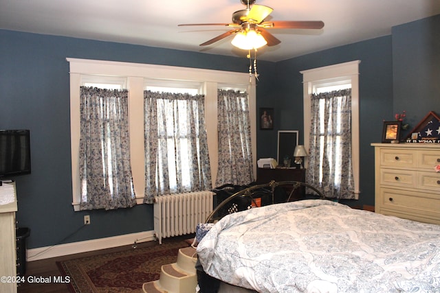 bedroom featuring multiple windows, dark hardwood / wood-style floors, ceiling fan, and radiator