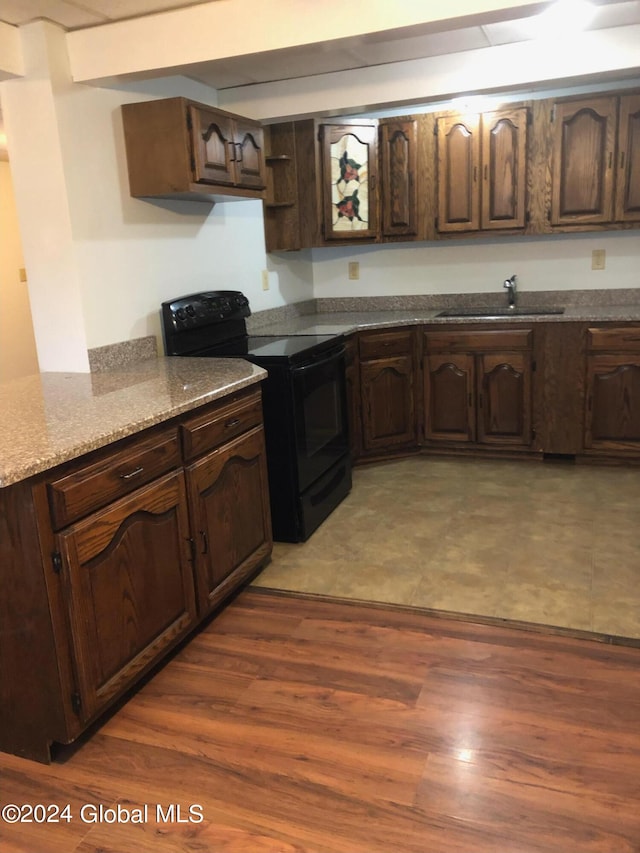 kitchen featuring light stone counters, dark brown cabinetry, hardwood / wood-style floors, black range with electric cooktop, and sink