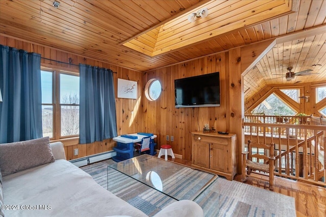 living room with wooden walls, a baseboard heating unit, ceiling fan, and wood-type flooring