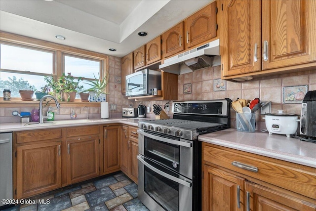 kitchen featuring dark tile floors, sink, a raised ceiling, appliances with stainless steel finishes, and tasteful backsplash