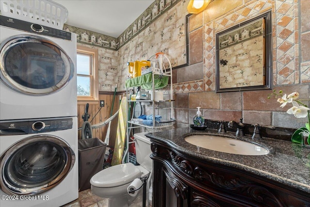 bathroom with toilet, large vanity, stacked washer and dryer, tasteful backsplash, and tile floors