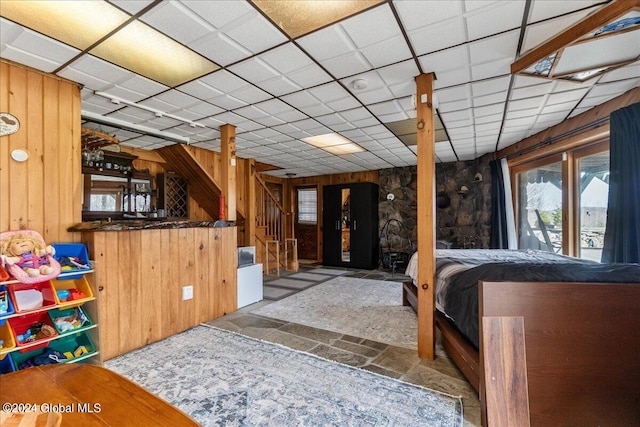 bedroom featuring light tile flooring, bar area, a paneled ceiling, and wood walls