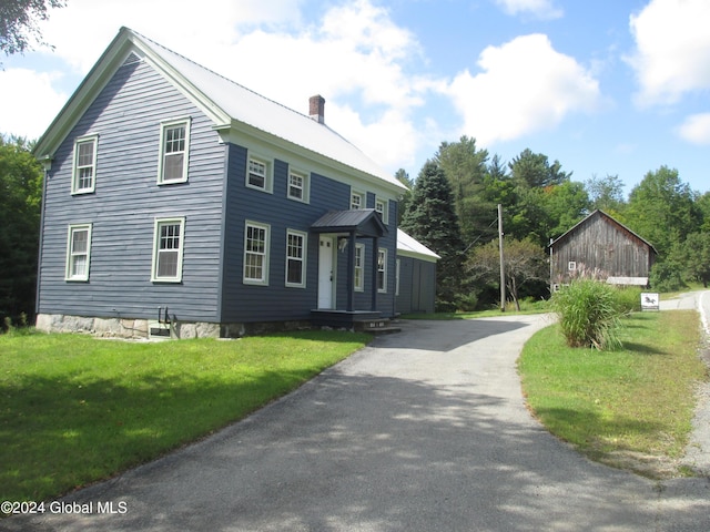 view of front of home with metal roof, a chimney, a front yard, and driveway