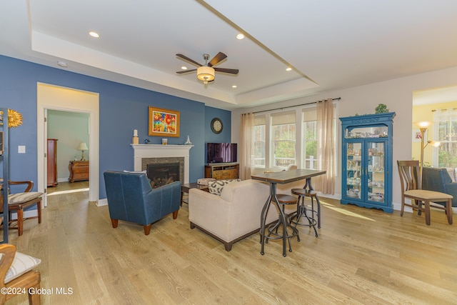 living area with a glass covered fireplace, a tray ceiling, light wood-style flooring, and recessed lighting