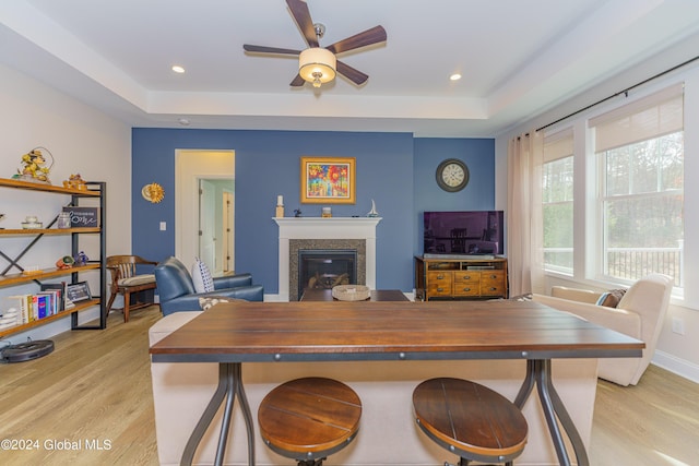 dining area featuring a glass covered fireplace, recessed lighting, a raised ceiling, and light wood-style floors