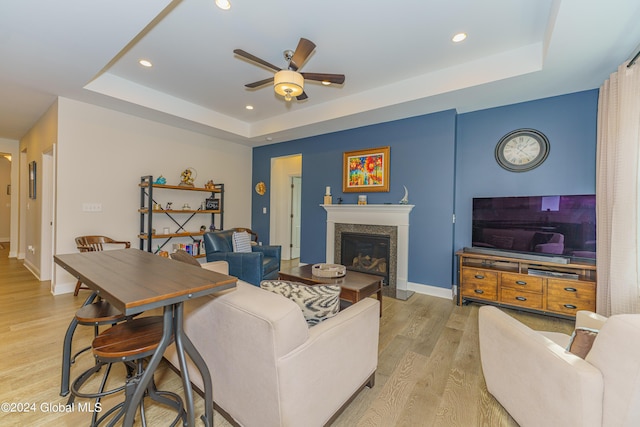 living room featuring a fireplace, baseboards, light wood-style floors, and a tray ceiling