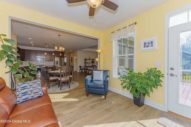 living room with ceiling fan with notable chandelier, baseboards, and light wood finished floors