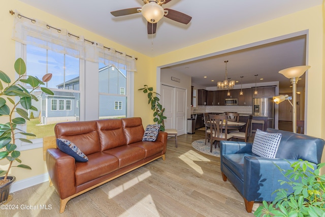 living area featuring baseboards, light wood-style flooring, and ceiling fan with notable chandelier