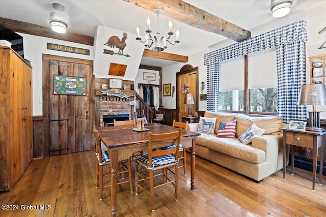 dining area featuring a brick fireplace, light hardwood / wood-style floors, an inviting chandelier, and beam ceiling