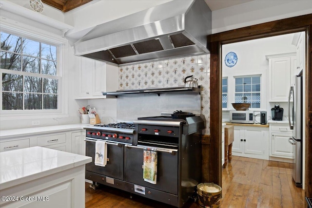 kitchen with wall chimney exhaust hood, white cabinetry, appliances with stainless steel finishes, and light hardwood / wood-style flooring