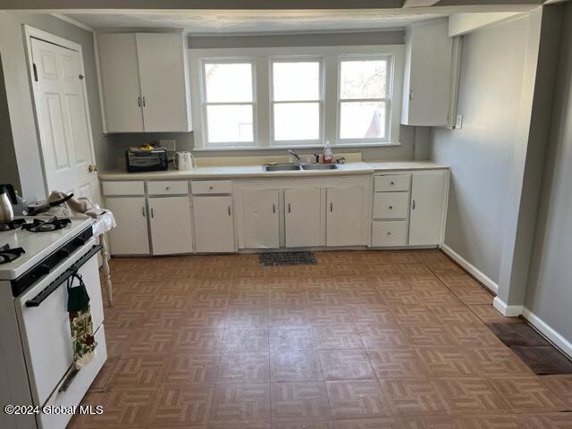 kitchen with sink, white cabinetry, light parquet floors, and white gas stove