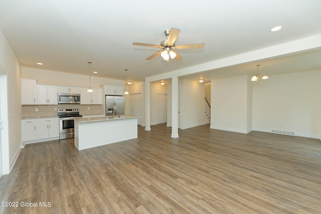 kitchen featuring stainless steel appliances, white cabinetry, decorative light fixtures, an island with sink, and light hardwood / wood-style flooring