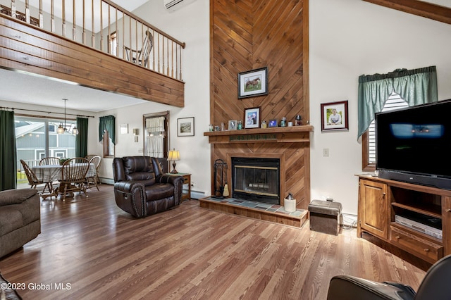 living room with a towering ceiling, a tile fireplace, a baseboard radiator, hardwood / wood-style floors, and an inviting chandelier