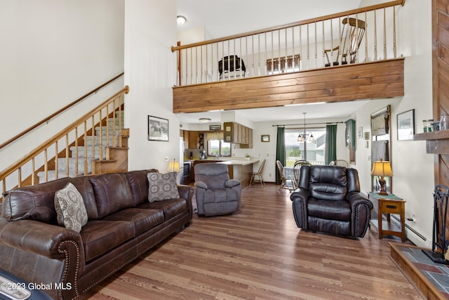 living room featuring wood-type flooring, a notable chandelier, a baseboard heating unit, and a high ceiling