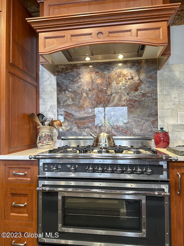 kitchen featuring tasteful backsplash, premium range hood, light stone countertops, and range with two ovens