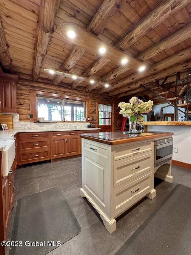 kitchen with oven, log walls, beam ceiling, wooden ceiling, and cream cabinets