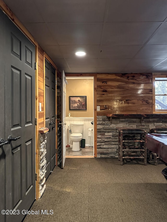 corridor featuring a paneled ceiling, dark colored carpet, and wood walls