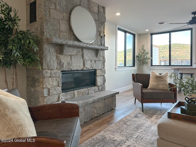 living room featuring ceiling fan, light hardwood / wood-style floors, and a stone fireplace