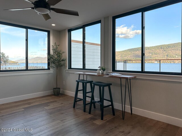 unfurnished dining area with ceiling fan, a water and mountain view, and wood-type flooring