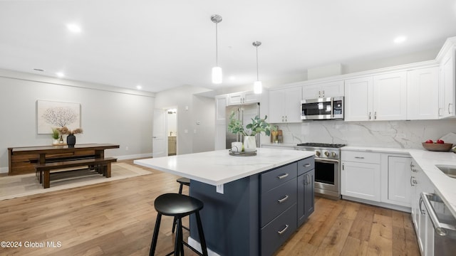 kitchen with high end appliances, hanging light fixtures, light wood-type flooring, a kitchen island, and white cabinetry